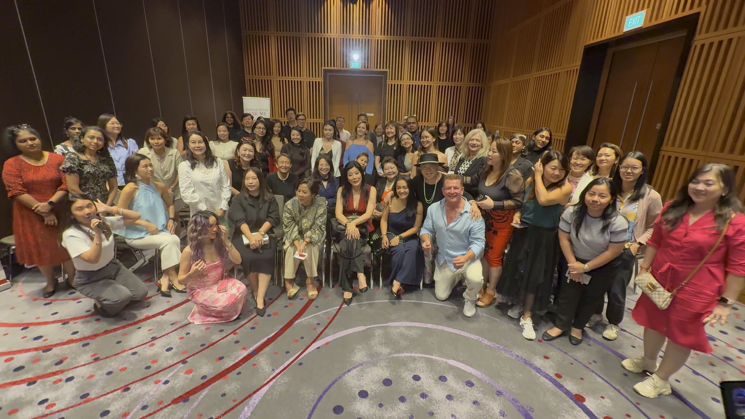 A large international group standing together in a hotel function room at the end of a session