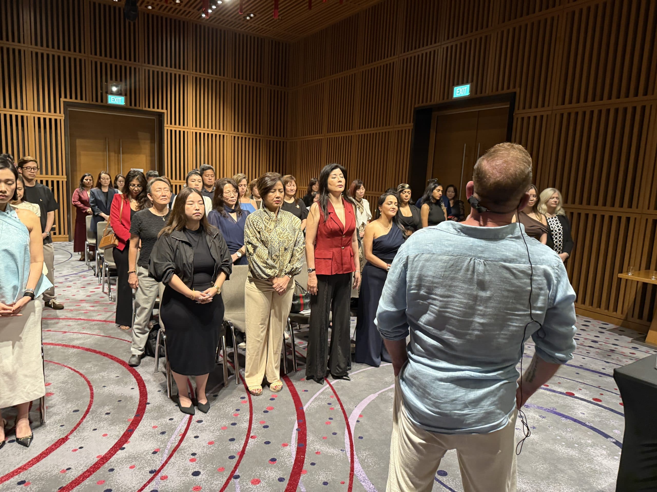 A room of professionals standing with their eyes closed, mid-process, Chris Howard working with them from the foreground