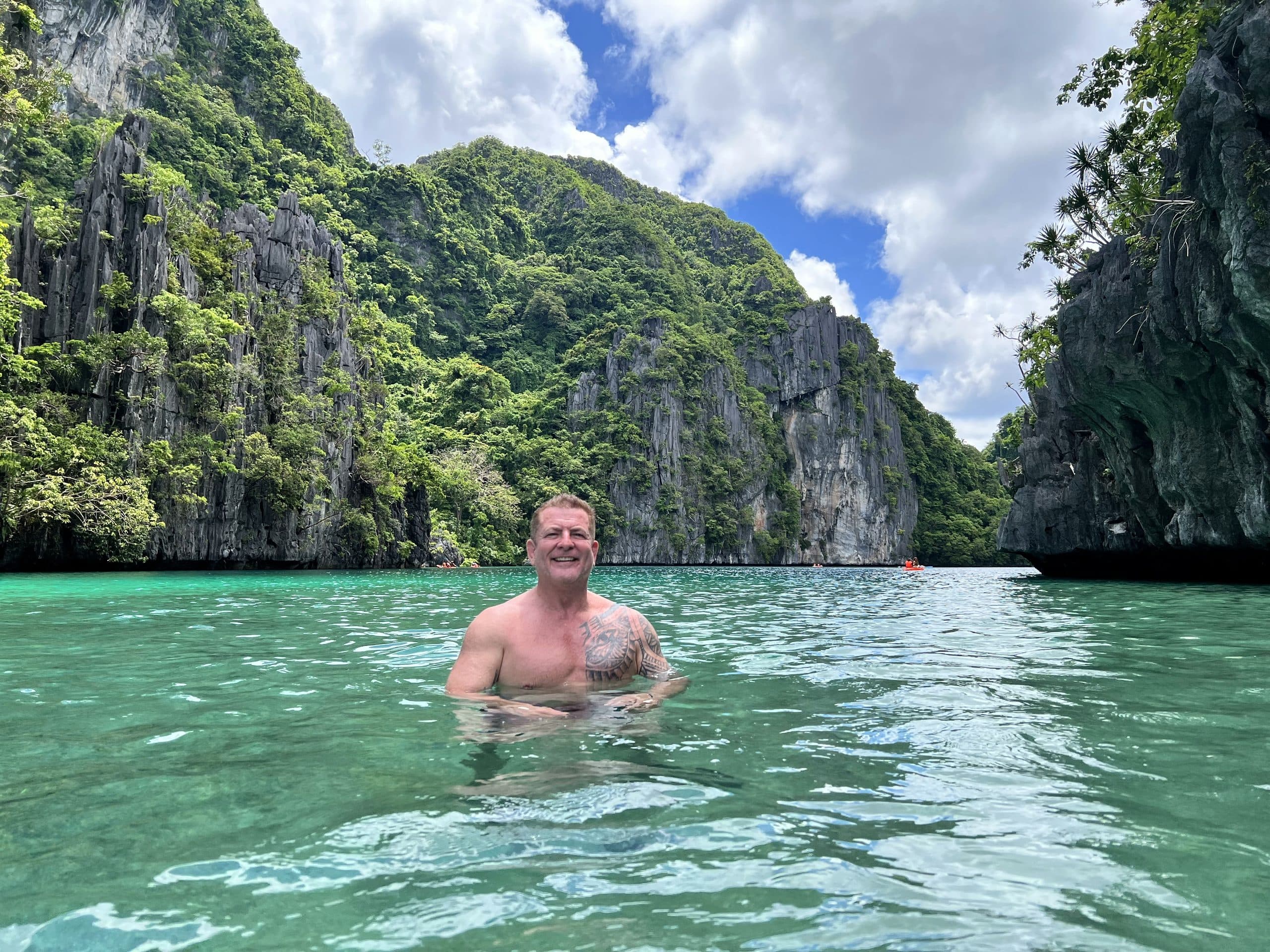 Chris Howard standing chest-deep in a turquoise lagoon at El Nido, limestone cliffs rising behind him
